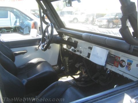 1990 Ford Bronco - Stripped interior of a vintage off-road 4x4 with white painted dash, black bucket seats, manual steering wheel and a padded roll cage.
