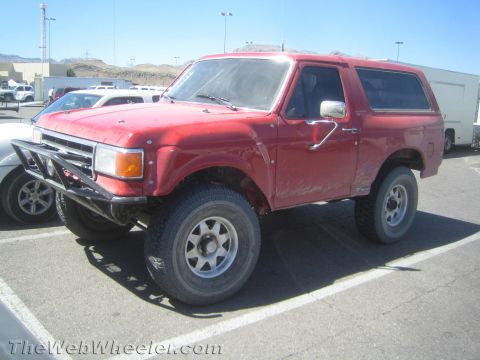 1990 Ford Bronco - Red lifted full-size Ford Bronco with tube front bumper and off-road tires parked on asphalt.