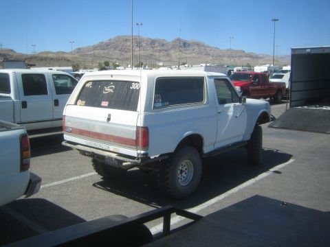 1990 Ford Bronco - Rear three-quarter view of a white lifted full-size Ford Bronco on off-road tires with desert mountains in the background.
