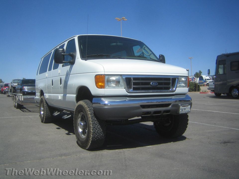 White lifted Ford E-series 4x4 passenger van with off-road tires in a lot