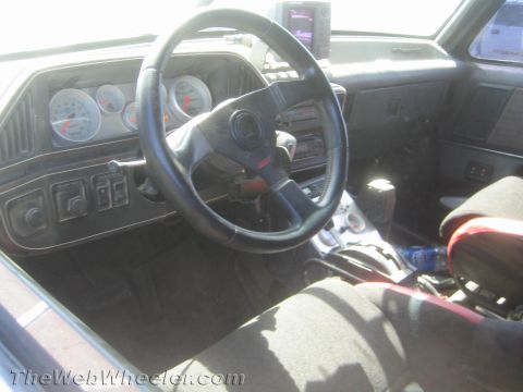 1990 Ford Bronco - Dashboard interior of a race vehicle with cluster of aftermarket gauges, sport steering wheel, shifter and harness-equipped seat.