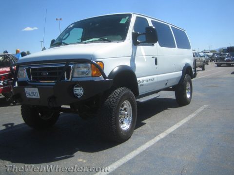 1990 Ford Bronco - white Ford Sportsmobile 4x4 van on a lift kit with brush guard, off-road tires and Hella lights parked in a lot.