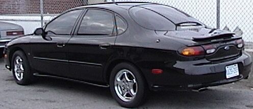 Black sedan, 1996 model year, with a spoiler and aftermarket wheels, seen from the rear three-quarter angle
