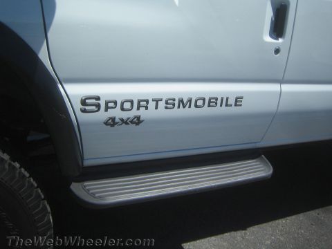 1990 Ford Bronco - Close-up of black Sportsmobile 4x4 lettering on the lower body of a silver van above the brushed running board.