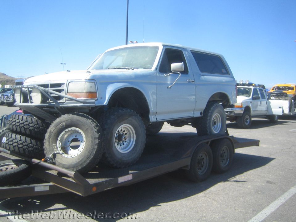 White full-size Ford Bronco with spare tires loaded on a flatbed trailer