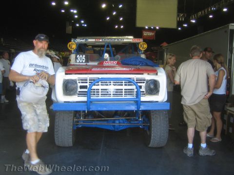 1990 Ford Bronco - white and blue Ford off-road race truck numbered 305 on display indoors as people and a man in a BFGoodrich shirt stand nearby.