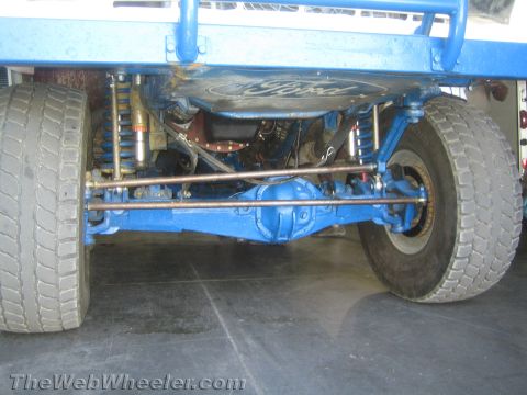 1990 Ford Bronco - Underbody view showing the blue front axle, shocks and tie rods of an off-road race truck with a Ford-stamped diff cover.