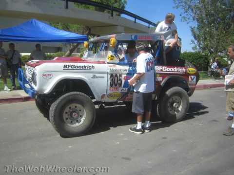 1990 Ford Bronco - white early Ford Bronco off-road race truck, number 805, with BFGoodrich graphics sits outdoors while crew members work on it.