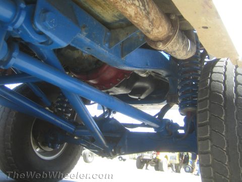 1990 Ford Bronco - Close underbody view of an off-road race truck showing blue suspension links, driveshaft, coilover shock and differential.