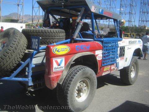 1990 Ford Bronco - Rear three-quarter view of a red-and-white early Ford Bronco off-road race truck, number 305, with mounted spare tires and DRW and Valvolin…
