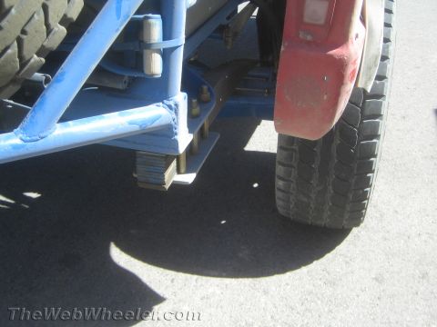 1990 Ford Bronco - Detail of the rear blue tube frame, stacked leaf springs and red fender with tires on an off-road race truck.