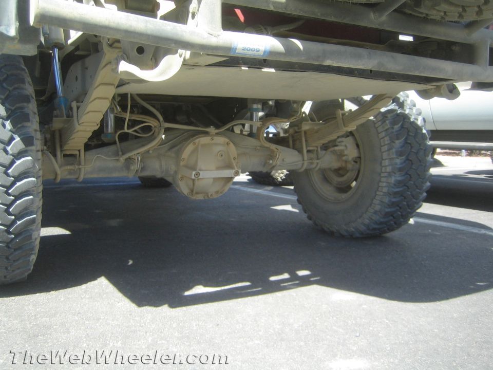 Underside of lifted off-road truck showing solid axle, leaf springs, exhaust and large tires