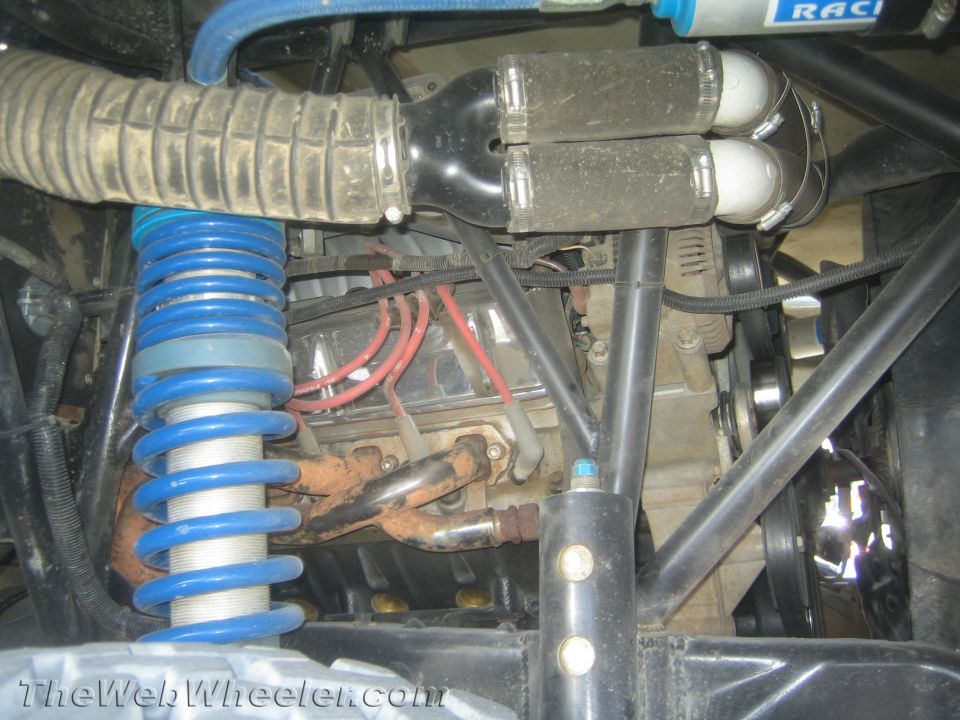 Engine bay of off-road truck with blue coilover, headers, plug wires and intake hose