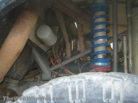 1990 Ford Bronco - blue King coilover shock sits among rusty suspension links above a muddy off-road tire beneath a truck.