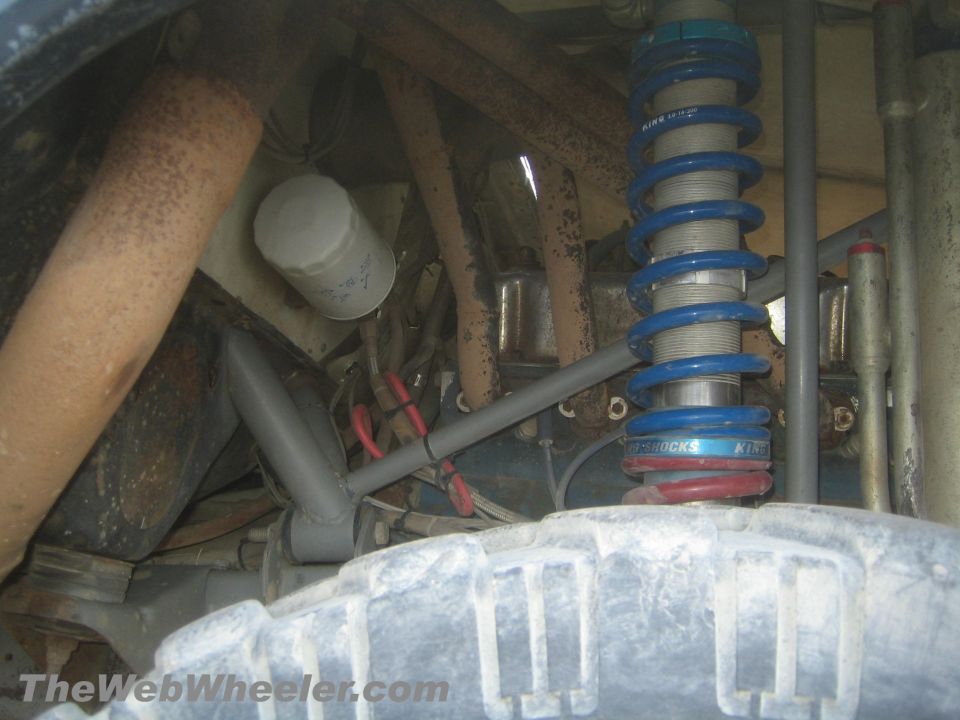 Blue King coilover shock and rusty suspension components above a muddy tire underneath a truck
