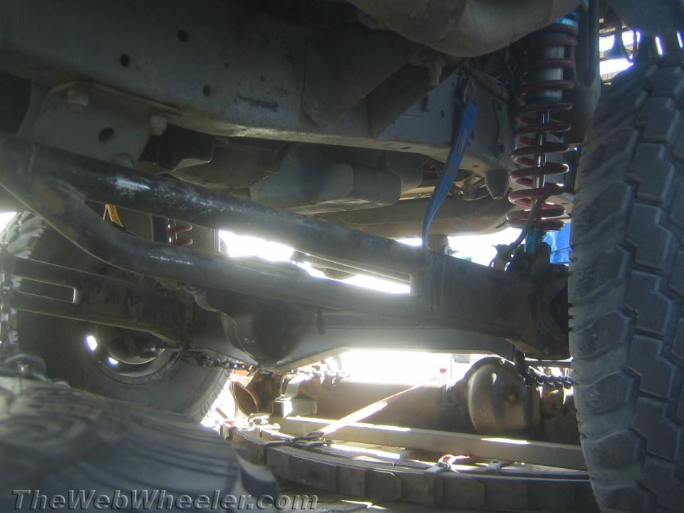 Wide underside view of a lifted truck showing axle, driveshaft, coilover and tires