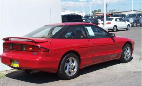 1996 Ford Probe - A red coupe with a spoiler and aftermarket wheels is parked on asphalt with other vehicles in the background.