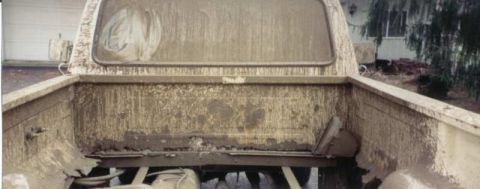1980 Ford F-250 - The rear of a heavily mud-caked 1973 Ford F-100 pickup truck, showing its damaged bed and missing tailgate.