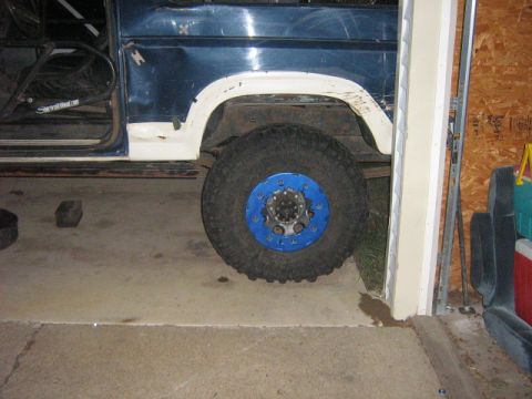 1986 Ford Bronco - Close-up of a 1986 Ford Bronco's side, highlighting its off-road tire and blue beadlock wheel.