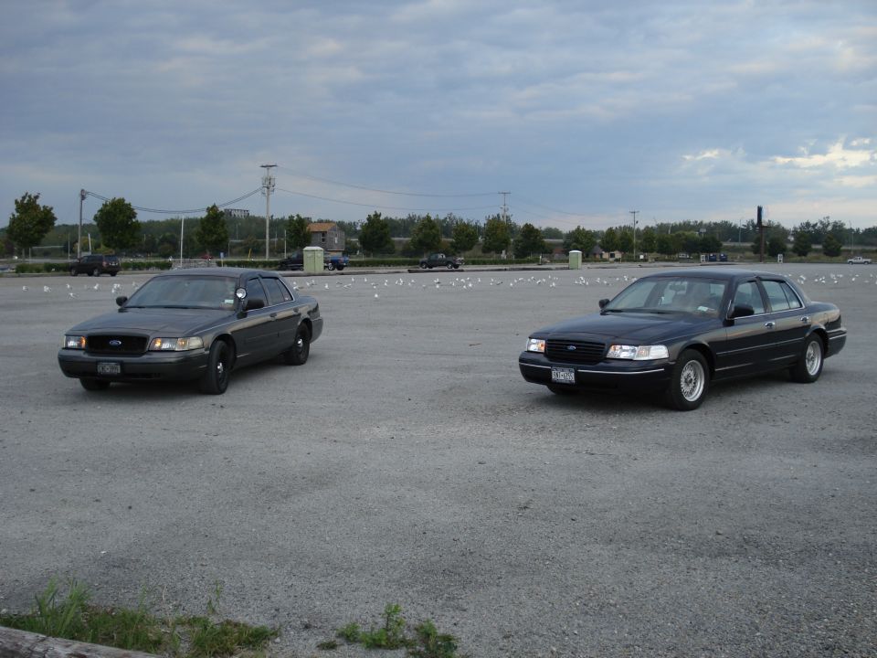 Gray police-package and dark blue Ford Crown Victoria sedans parked in an empty gravel lot
