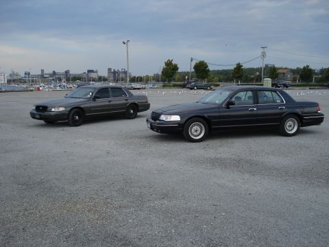 2000 Ford Crown Victoria - Two Ford Crown Victoria police cars are parked in an outdoor lot with a marina and city skyline in the distance.