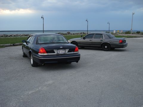 2000 Ford Crown Victoria - Two Ford Crown Victorias parked near a body of water under a cloudy sky.