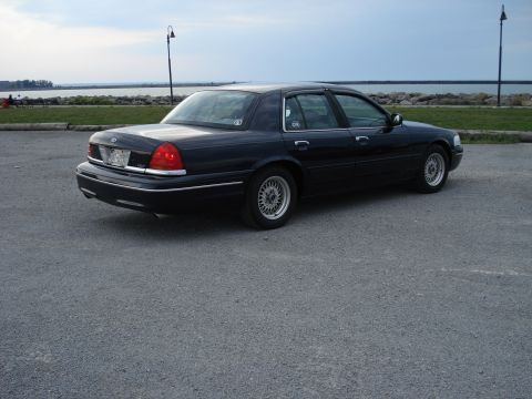 2000 Ford Crown Victoria - A dark 2000 Ford Crown Victoria is seen from the rear three-quarter angle, parked on an asphalt surface near a body of water.