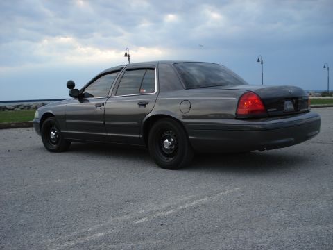 2000 Ford Crown Victoria - A dark gray Ford Crown Victoria Police Interceptor is parked by the water under a cloudy sky.