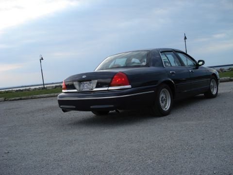 2000 Ford Crown Victoria - A black 2000 Ford Crown Victoria is parked outdoors on a cloudy day, with a body of water in the background.