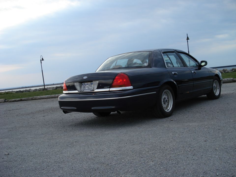 Rear three-quarter view of dark Ford Crown Victoria sedan on waterfront lot