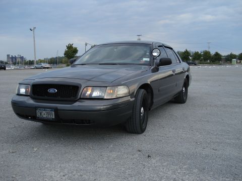 2000 Ford Crown Victoria - A dark gray 2000 Ford Crown Victoria is parked in a gravel lot under an overcast sky.