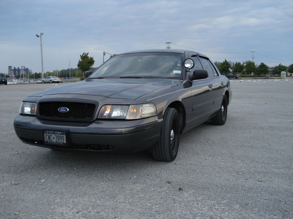 Gray Ford Crown Victoria Police Interceptor with pillar spotlight and steel wheels on a gravel lot