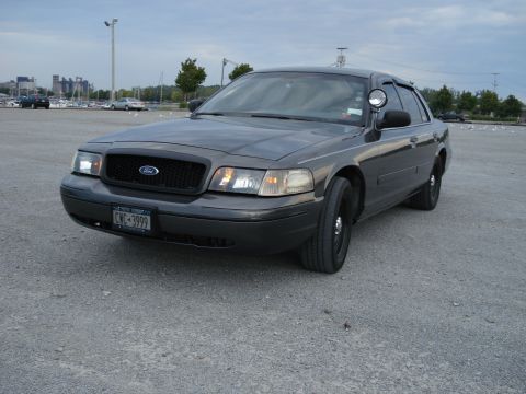 2000 Ford Crown Victoria - Ford Crown Victoria police car with black grille and wheels, seen from the front 3/4 angle.