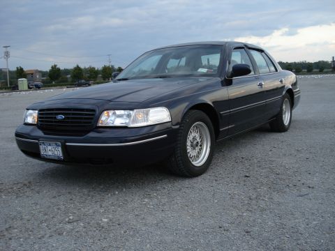 2000 Ford Crown Victoria - A dark Ford Crown Victoria is parked on a gravel lot under a cloudy sky.