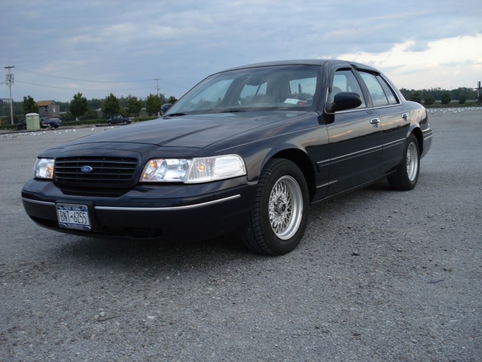 Navy Ford Crown Victoria sedan, front 3/4 view, wire wheels, NY plate BNY-6255, on gravel lot.