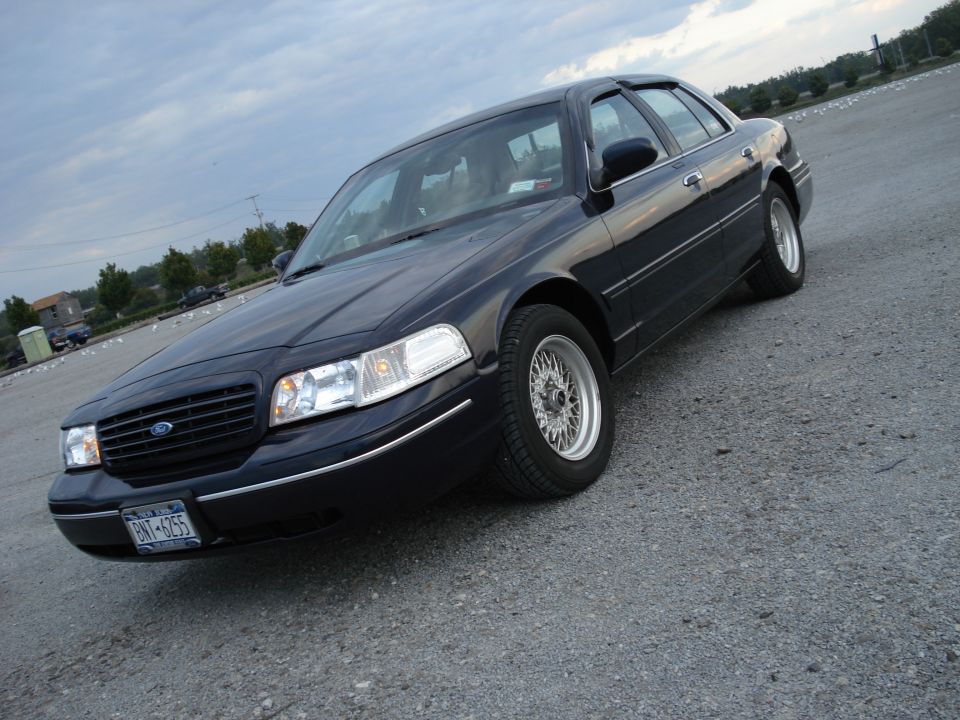 Dark blue Ford Crown Victoria sedan with wire wheels on gravel lot