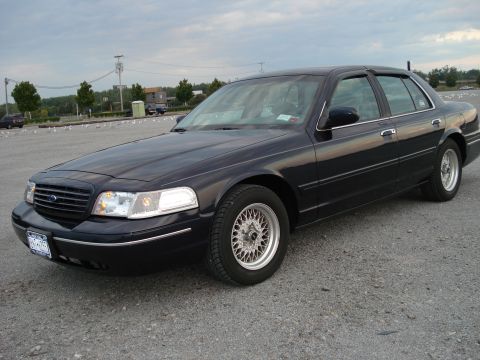 2000 Ford Crown Victoria - A black 2000 Ford Crown Victoria is parked in an outdoor lot under a cloudy sky.