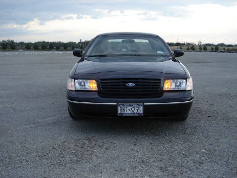 2000 Ford Crown Victoria - A dark sedan is parked on a gravel lot under a cloudy sky.