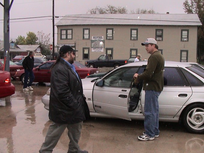 Two guys standing by a silver sedan with its door open, in front of a hotel