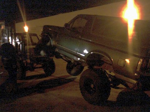 1996 Ford Bronco - A dark-colored pickup truck is shown lifted with large tires, parked outdoors at night.
