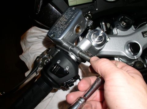 1990 Ford Bronco - A hand uses a wrench to work on the brake fluid reservoir and controls on a motorcycle handlebar.