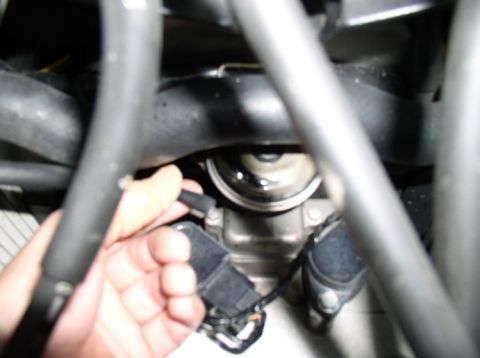 1990 Ford Bronco - Close-up view of a hand disconnecting an electrical connector from an engine part, with hoses and other engine components visible.