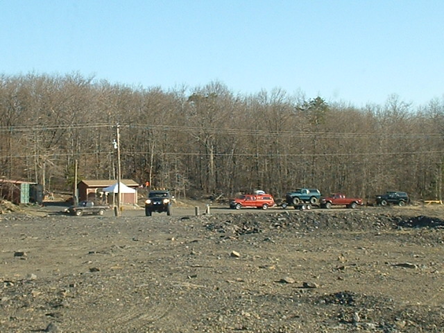 Several off-road vehicles parked in a gravel lot with trees in the background