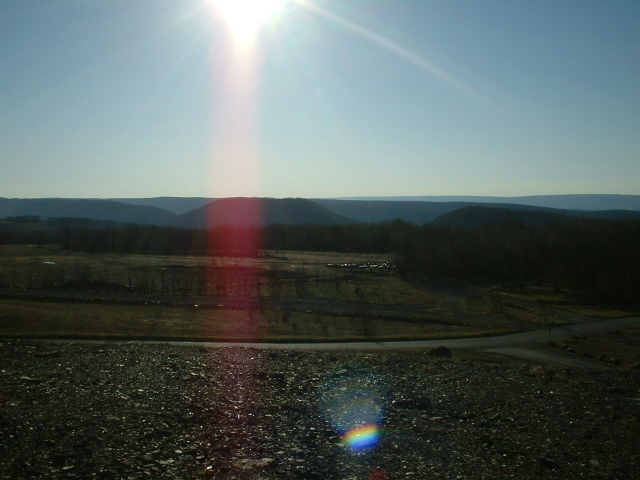 Sunny day over rolling hills and fields, with a bright sun flare in the sky