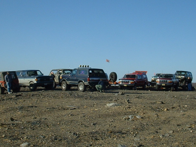 Several SUVs and trucks parked on rocky ground, one with a spare tire mounted on the back