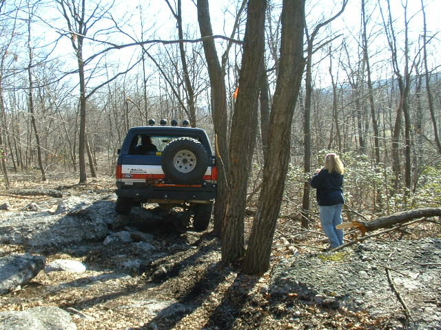 Blue and red Ford Bronco II with spare tire on rear, driving on rocky terrain