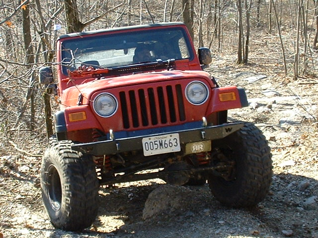 Red 2003 Jeep Wrangler with large tires on a rocky trail, front view