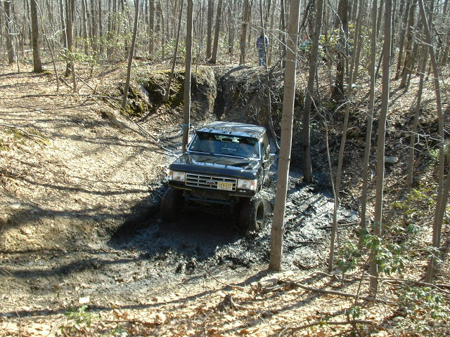 Black 1980s Ford Bronco off-roading through mud