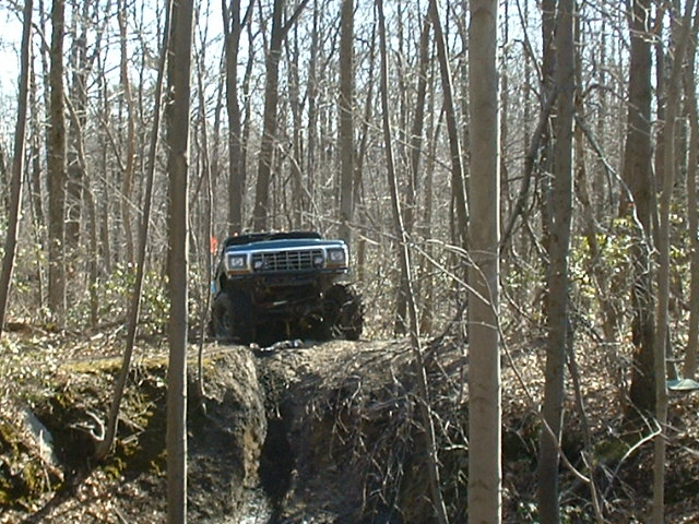 Blue pickup truck with large tires driving on a muddy incline in a forest