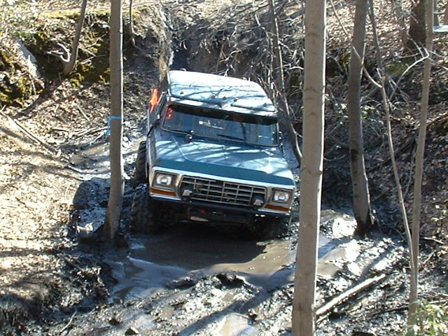 Blue 1978 Ford Bronco off-roading through mud and trees